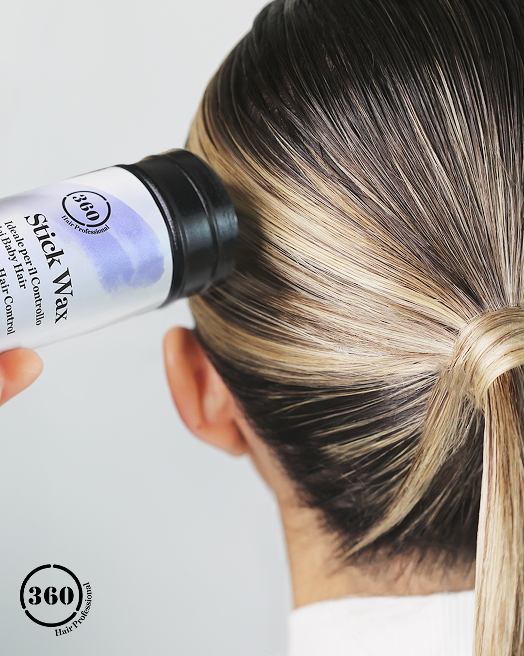 A close-up of a person's head from the back, showing dark brown to black hair with blonde highlights, while a hand holds a bottle of 360 Stick Nax Hair Color Primer against the hair. The 360 Stick Nax logo is visible on the bottle and as an overlay in the bottom-left corner.